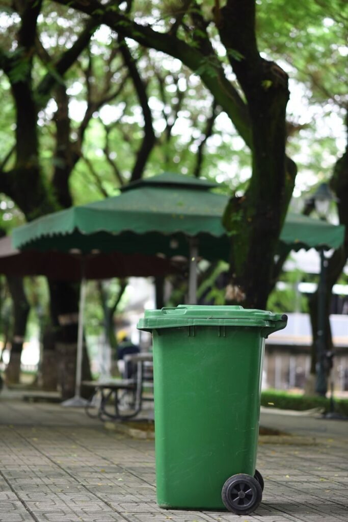 A vibrant green trash bin stands out in a leafy urban park, conveying eco-friendly waste management.